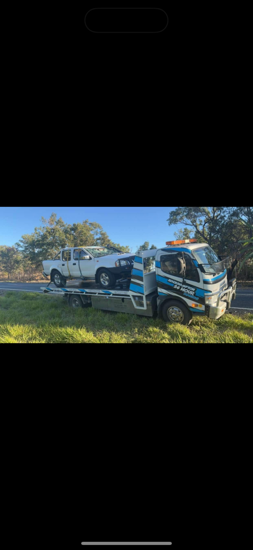 A white pickup truck being towed by a tow truck on a grassy roadside.— Fitzroy Towing & Transport in Parkhurst, QLD