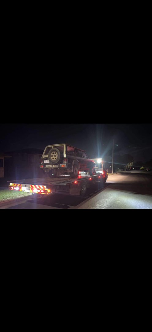 A truck towing a vehicle on a trailer at night. Tail lights and lights from trailer are lit.— Fitzroy Towing & Transport in Parkhurst, QLD