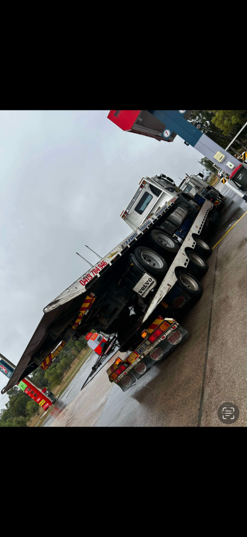 A large truck on the side of the road with a tilted trailer under a cloudy sky.