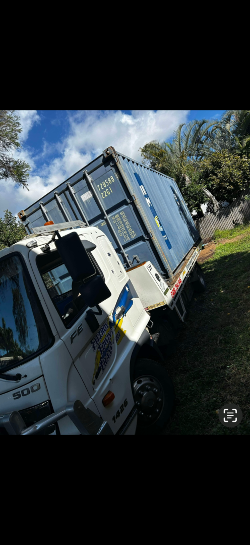 A blue shipping container loaded on a white truck on a grassy area under a blue sky.— Fitzroy Towing & Transport in Parkhurst, QLD
