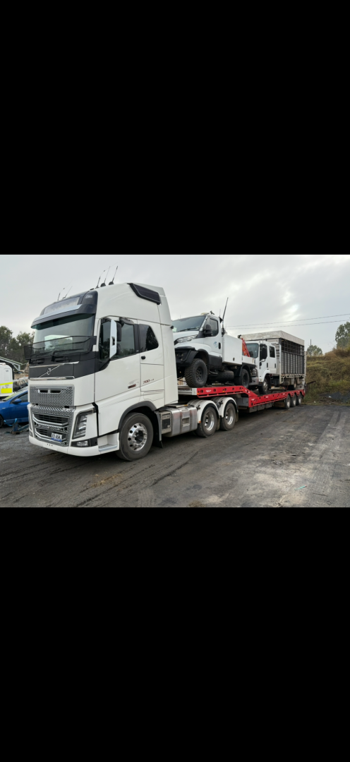 A white semi-truck carrying two vehicles on a flatbed trailer is parked outdoors.— Fitzroy Towing & Transport in Parkhurst, QLD