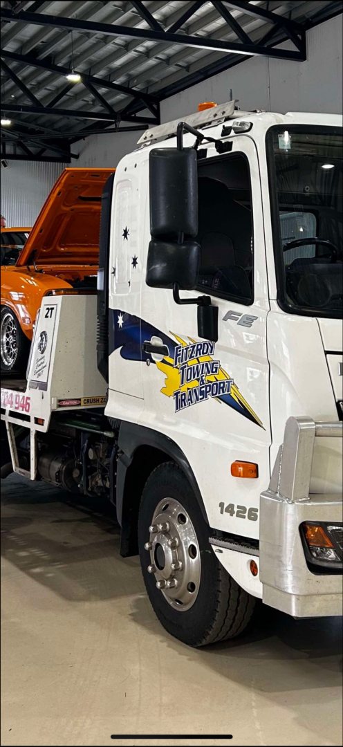 White tow truck carrying an orange car. The truck has the business name 