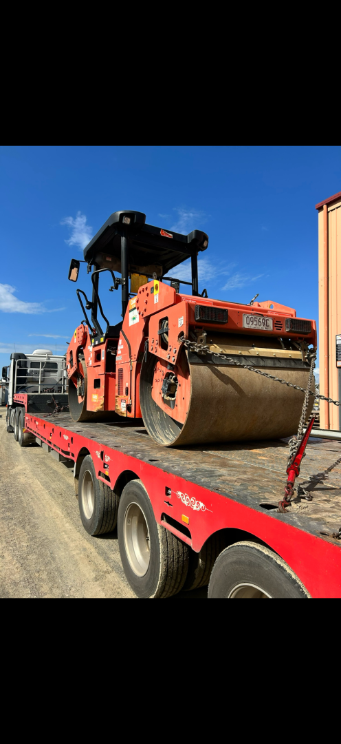 An orange road roller on a red flatbed trailer against a blue sky.— Fitzroy Towing & Transport in Parkhurst, QLD