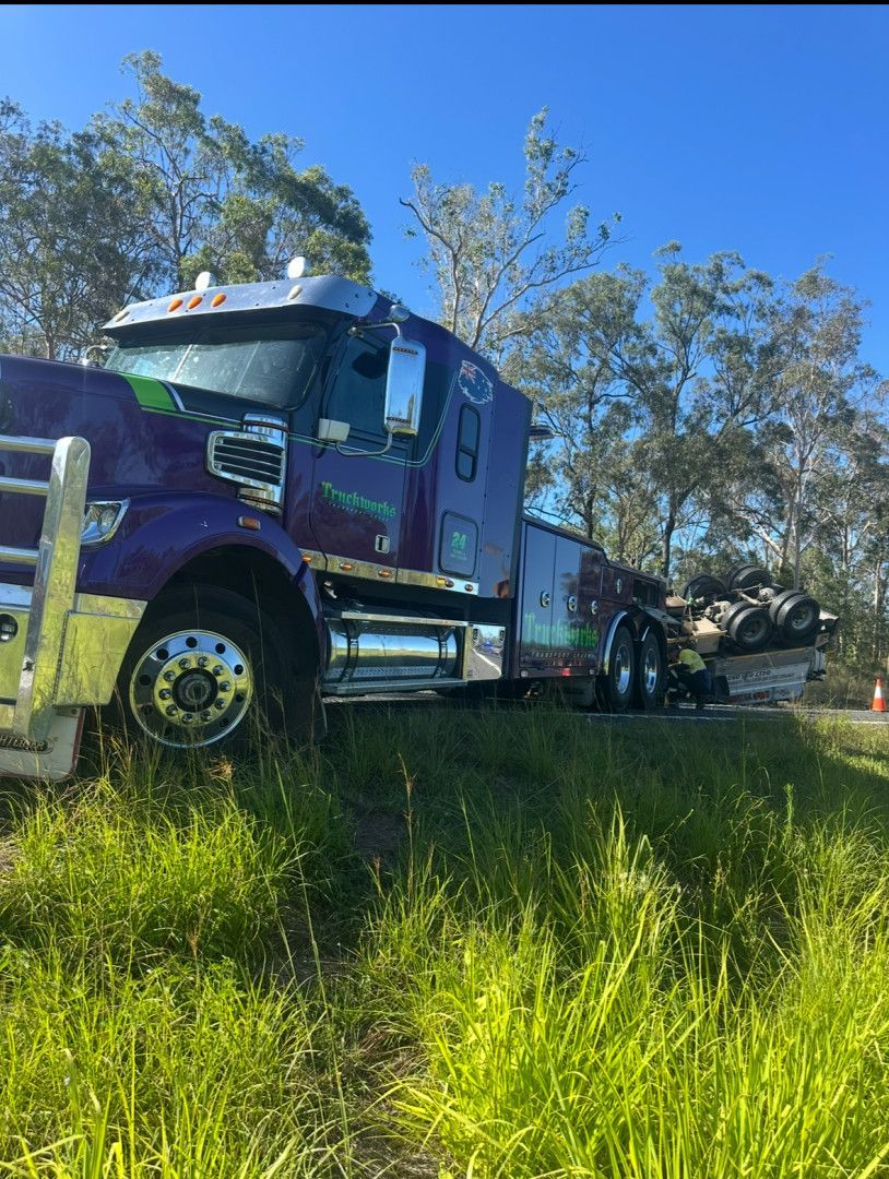 Purple semi-truck off road in tall green grass, under blue sky.— Fitzroy Towing & Transport in Parkhurst, QLD