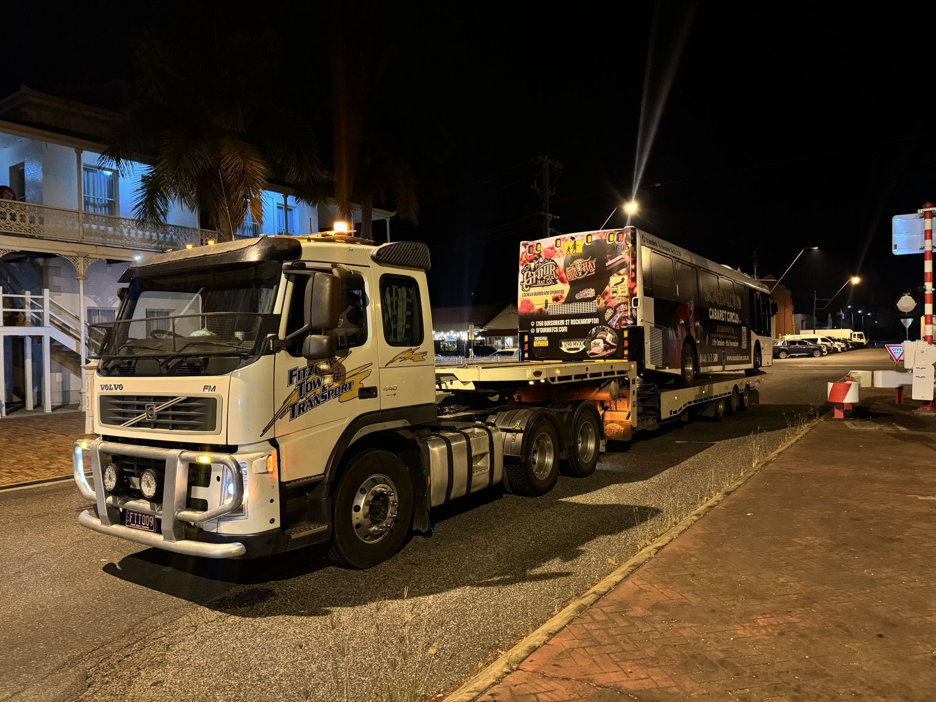White Volvo truck with trailer on a street at night. The trailer has event advertising.— Fitzroy Towing & Transport in Parkhurst, QLD