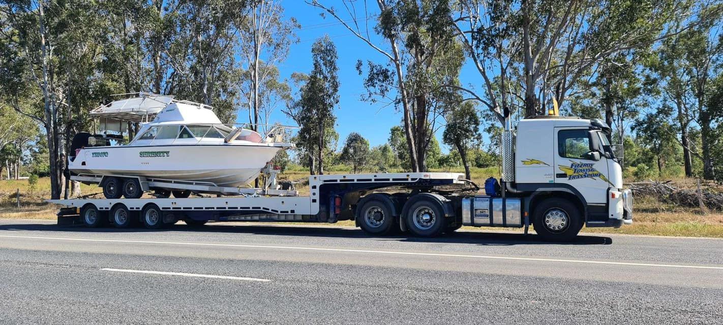 A Truck Towing a White Boat on a Flatbed Trailer — Fitzroy Towing & Transport in Parkhurst, QLD