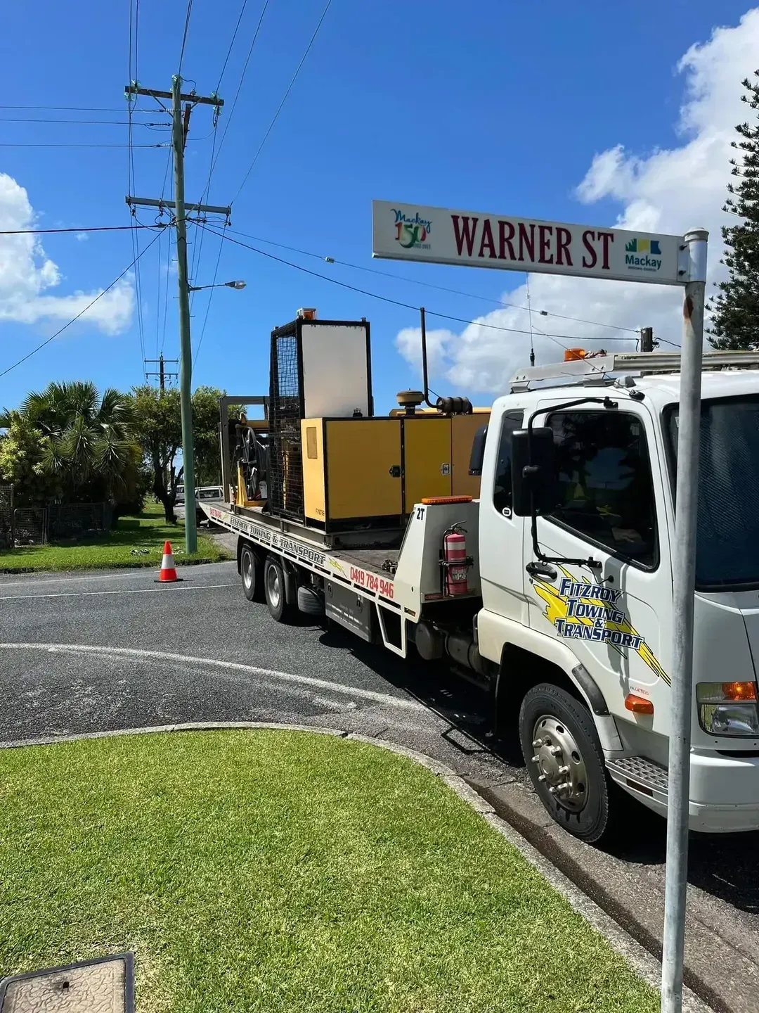 A Truck Hauling Yellow Machinery on a Flatbed Trailer — Fitzroy Towing & Transport in Biloela, QLD