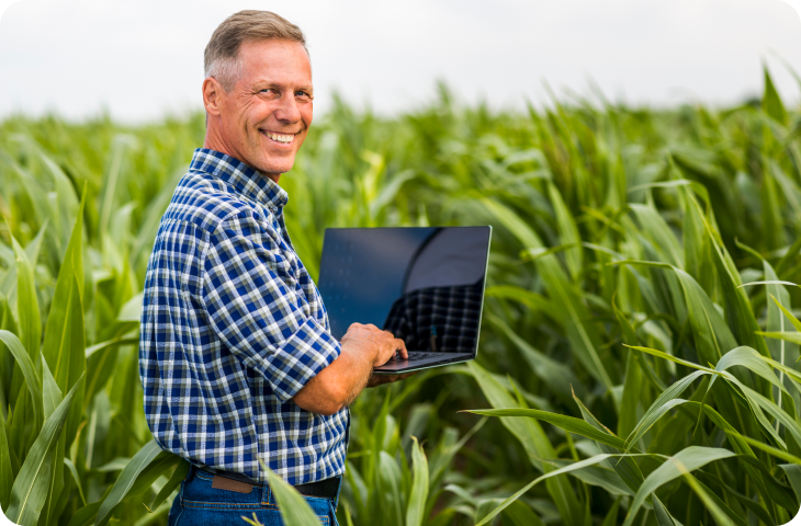 Um homem está parado em um campo segurando um laptop.