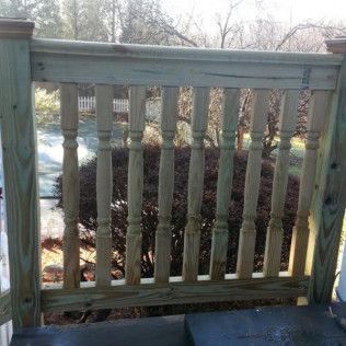 Wooden deck railing with vertical balusters, surrounded by foliage and trees.