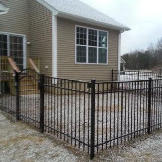 Black metal fence around a patio outside a tan house with snow on the ground.