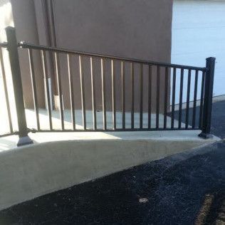 Black metal railing on a concrete foundation in front of a brown wall and a white door.