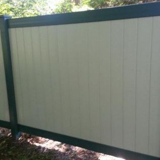Cream-colored vertical panel fence with dark green trim in a wooded setting.