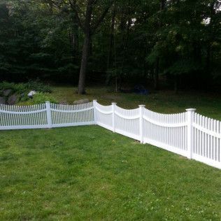 White picket fence encloses a green lawn, trees in the background.