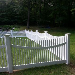 White picket fence in a grassy yard with trees in the background.