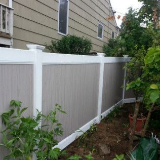 White and gray privacy fence in a backyard with green bushes and a house.