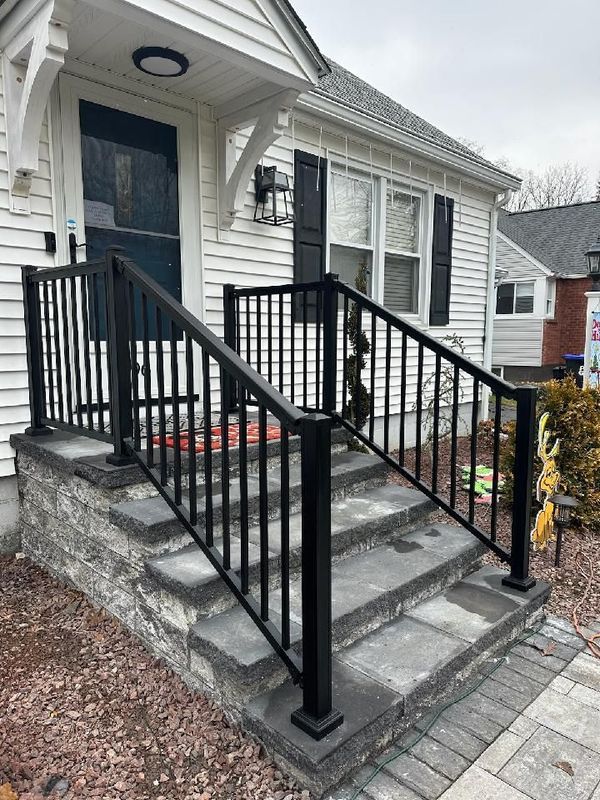 Two-story house with white deck, steps, and railing. Light tan siding, green lawn, white door.