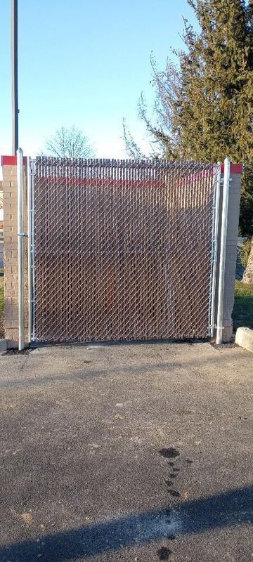 A metal chain-link fence encloses an area with a paved ground and blue sky backdrop.