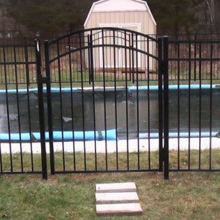 Black metal pool fence with arched gate. Green grass, blue pool cover.