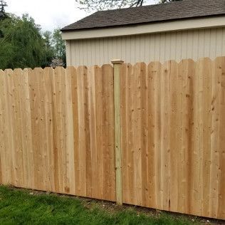 Wooden fence with scalloped top in a backyard, light brown wood.