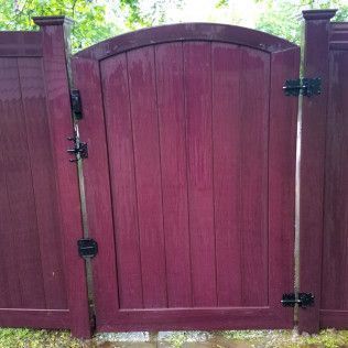 Burgundy wooden gate in a matching fence, with black hardware and a rounded top.