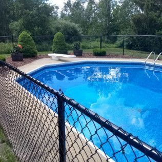 Pool with blue water and white diving board, surrounded by a black chain link fence. Green trees in background.