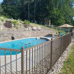 Pool fenced with brown metal bars, surrounded by grass and trees.