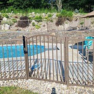 Pool gate with brown metal bars. The pool is surrounded by a fence on a sunny day.