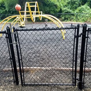 Black chain-link gate open in a playground with yellow climbing equipment.