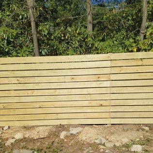 Wooden horizontal slat fence in front of trees.