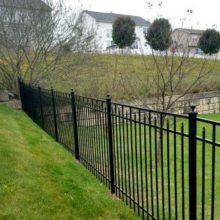 Black metal fence on a grassy slope, with homes and trees in the background.