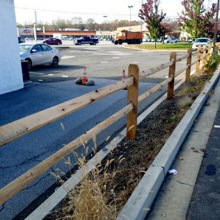 A split-rail fence borders a parking lot, with cars and a truck in the background.