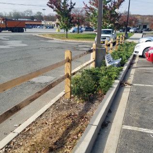 Parking lot with a wooden fence, shrubs, bench, and cars.