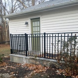 Black railing in front of a white building with a green door. Fallen leaves are on the ground.