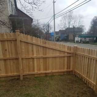 Wooden fence enclosing a grassy yard, with a street and houses in the background.