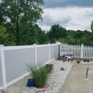 Backyard with grey and white fences, pool, trees, and a cloudy sky.