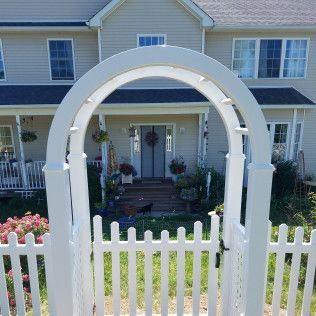 White picket fence with gate and arched trellis leading to a house entrance.
