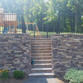 Stone steps lead up to a black fence and gate in a backyard.