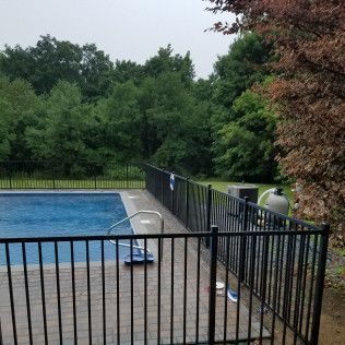 Pool surrounded by black fence with trees in the background on a cloudy day.
