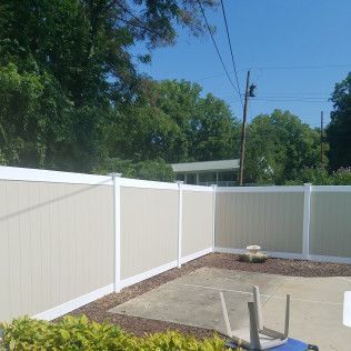 Tan and white vinyl privacy fence surrounding a small concrete patio. Green bushes in foreground.