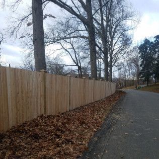 Wooden fence lines a road with bare trees and fallen leaves.