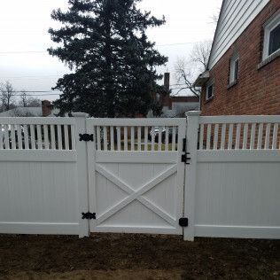 White vinyl fence with a gate. A brick house is in the background.