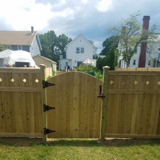 Wooden gate with black hinges and latch, set in a wooden fence. Houses in background.