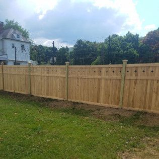 Wooden fence in front of a house, set on green grass, with a cloudy sky in the background.