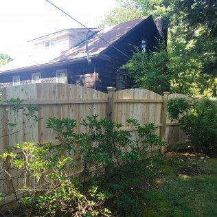 Wooden fence in front of a dark house with overgrown bushes.