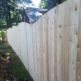 A light-colored wooden fence with a scalloped top. A house and trees are in the background.