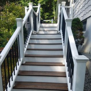 White and black staircase with brown steps leading upwards, outside a white house.