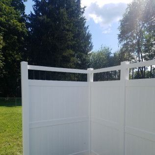 White vinyl fence corner in a sunny backyard with trees.