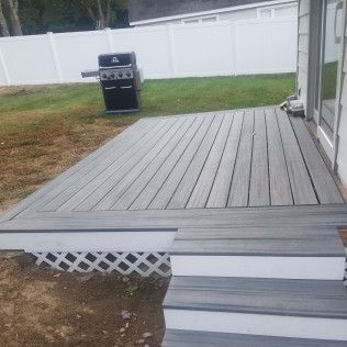 Gray composite deck with white lattice skirting and steps; grill on lawn, white fence.