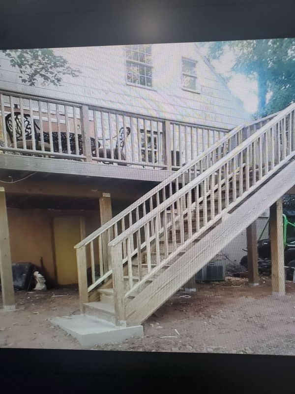 Wooden deck and staircase attached to a two-story house; viewed outdoors.