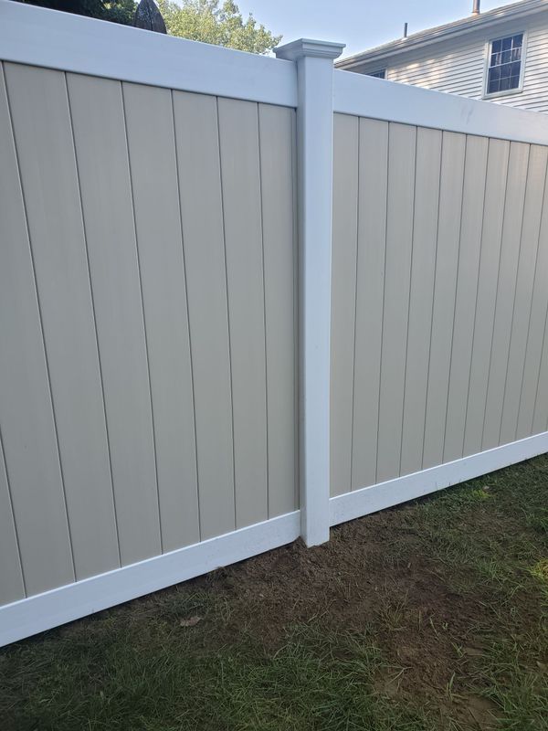 Tan vertical panel fence with white trim, against a green lawn.